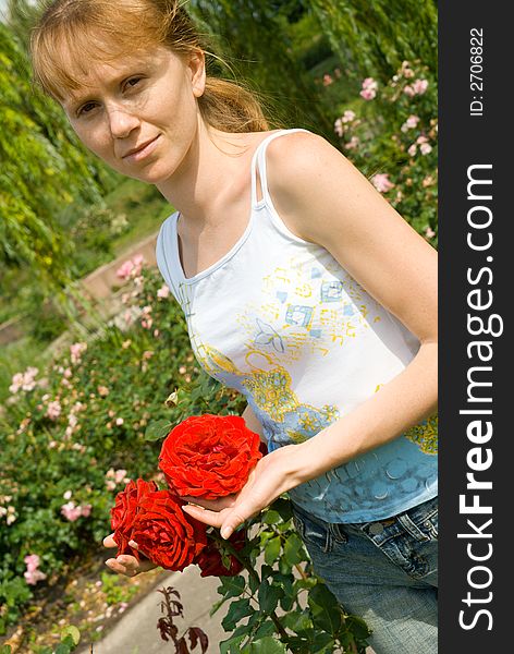 The red girl costs in a garden and holds in hands of a rose. The red girl costs in a garden and holds in hands of a rose
