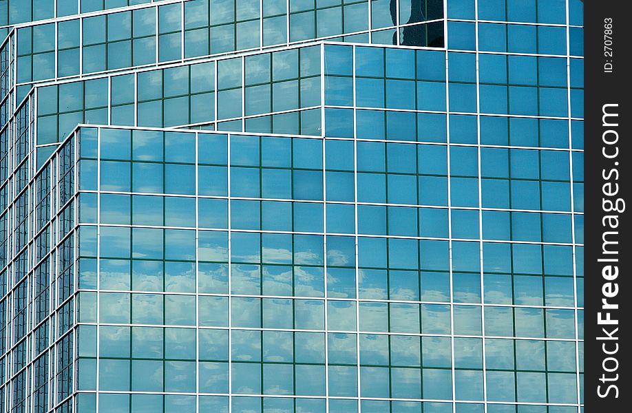 Reflection of a blue sky and clouds in the mirrored glass of a tall office building. Reflection of a blue sky and clouds in the mirrored glass of a tall office building.