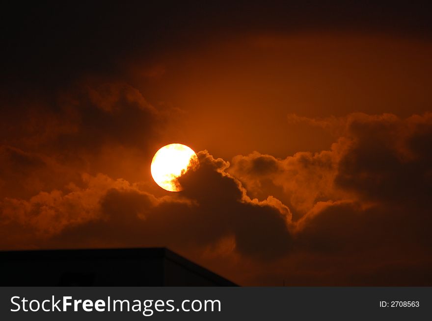 A sun going down in the evening over a town scene with clouds, sunset. A sun going down in the evening over a town scene with clouds, sunset