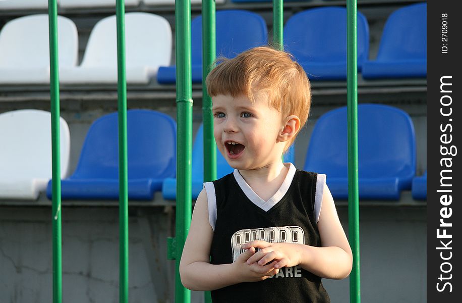 The fair-haired boy shouts about a fencing of tribunes in stadium. The fair-haired boy shouts about a fencing of tribunes in stadium