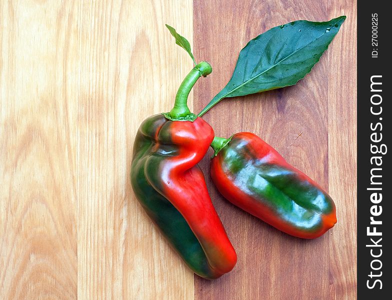 Two variegated peppers on wooden cutting board. Two variegated peppers on wooden cutting board.