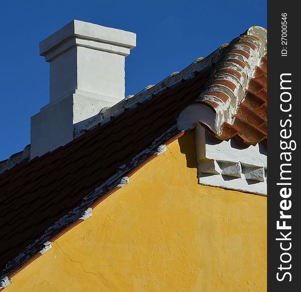 Behind the classic yellow gable, a chimney on the rooftop of red tiles is seen with the characteristic white paint decoration of Skagen, Denmark. Behind the classic yellow gable, a chimney on the rooftop of red tiles is seen with the characteristic white paint decoration of Skagen, Denmark