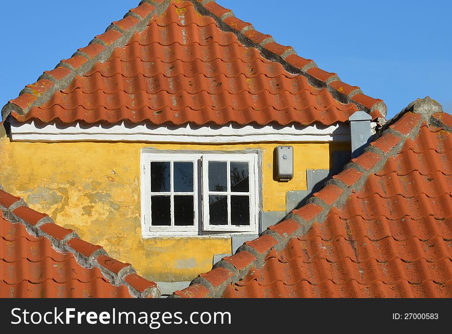 A triangular brick gable with yellow plaster and a white window is surrounded by triangular red tile roofs. A triangular brick gable with yellow plaster and a white window is surrounded by triangular red tile roofs