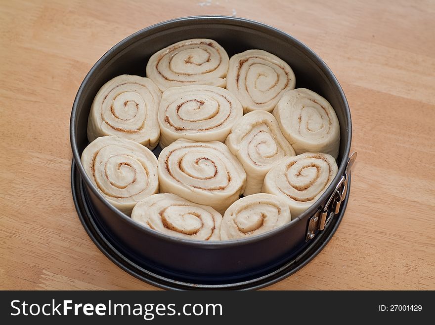 A sweet cinnamon roll cake in a baking form rising and waiting for the baking. A sweet cinnamon roll cake in a baking form rising and waiting for the baking.