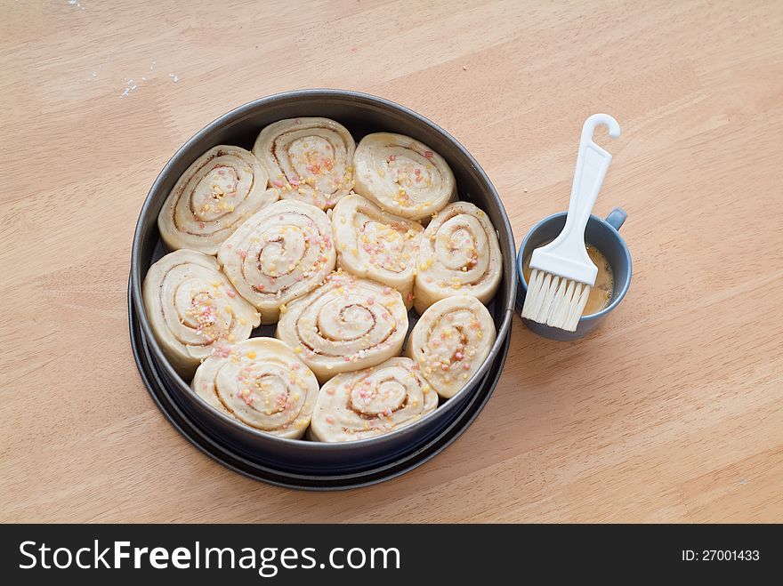 A decorated sweet cinnamon roll cake in a baking form rising and waiting for the baking. A decorated sweet cinnamon roll cake in a baking form rising and waiting for the baking.