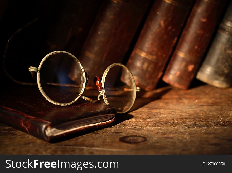 Old spectacles on leather notebook on background with old books