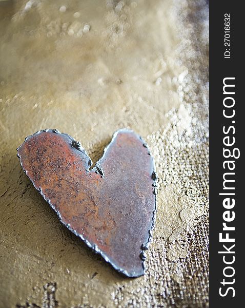 Handmade steel heart on golden hand painted burlap texture shot in natural light in a vertical format with copy space suitable for valentine. Handmade steel heart on golden hand painted burlap texture shot in natural light in a vertical format with copy space suitable for valentine