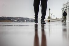 A Man Walks On Wet Asphalt In The Rain. A Park On The Seashore. A Muddy Reflection On The Ground. Royalty Free Stock Images