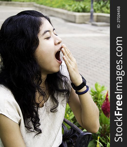 Young beautiful brunette woman yawning at outdoor garden