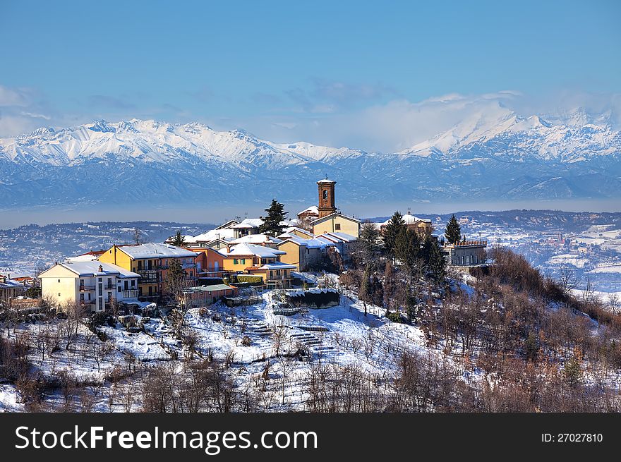 Small town on the hill and snowy mountain peaks on background in Piedmont, Northern Italy at winter. Small town on the hill and snowy mountain peaks on background in Piedmont, Northern Italy at winter.