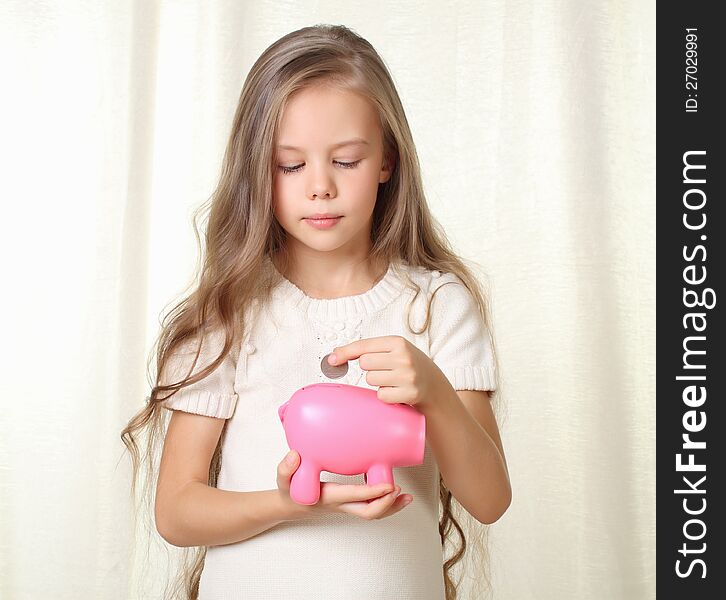 Little blond girl puts coin into piggy moneybox and dreaming about future purchase