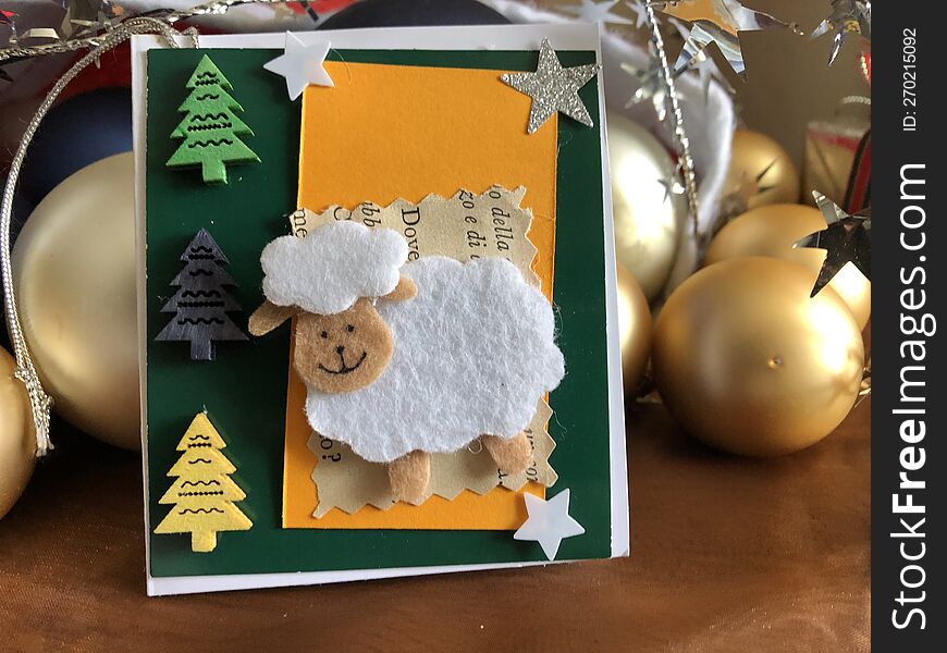 small christmas gift-tag, made with glossy white  photographic paper, green and orange cardboard, wood and metal elements and in the center a cotton made small decorative sheep