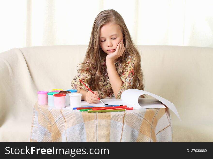 Little blond girl drawing at home on sofa