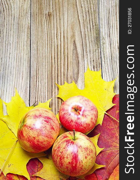 Apples and autumn maple leaves on a wooden background