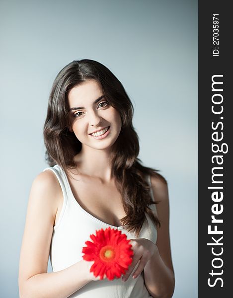 Portrait young attractive cheerful smiling casual caucasian girl with red gerbera flower on gray background. Portrait young attractive cheerful smiling casual caucasian girl with red gerbera flower on gray background