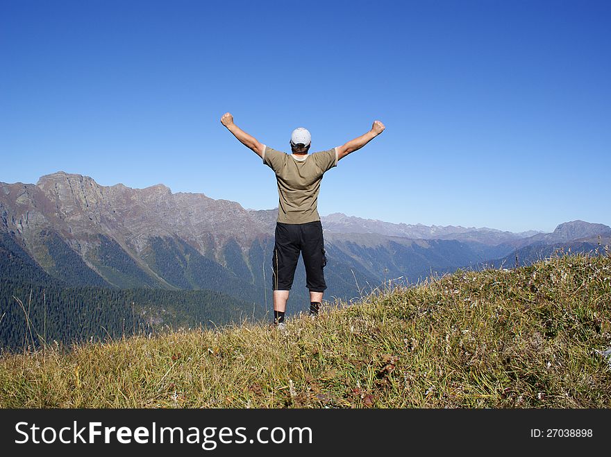 A man stands on a hillside with their hands up. A man stands on a hillside with their hands up