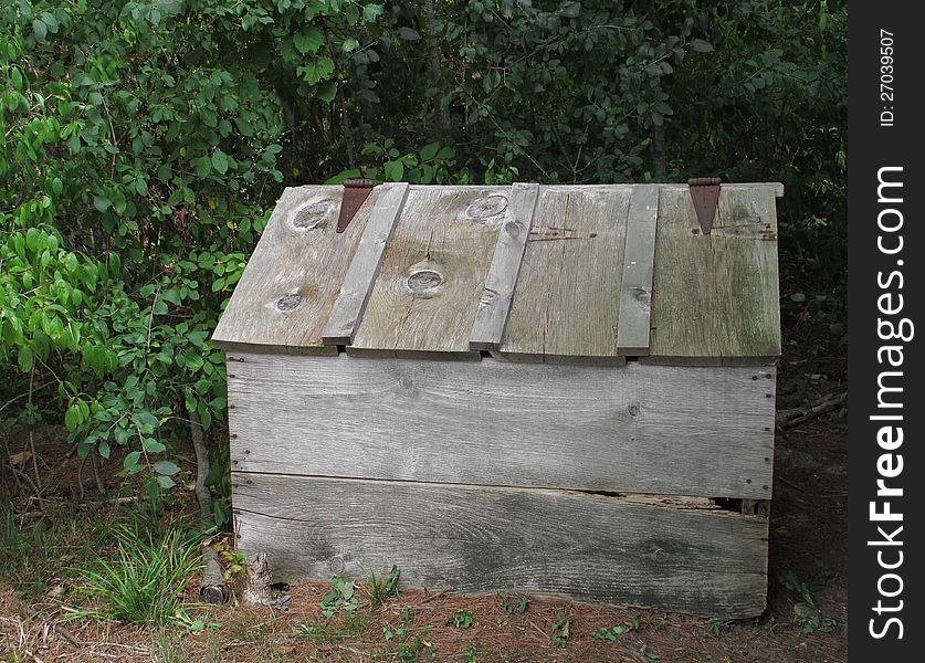 Old, weathered, and worn gray wooden outside storage box with hinged slanted lid, sitting in the bushes. Old, weathered, and worn gray wooden outside storage box with hinged slanted lid, sitting in the bushes.