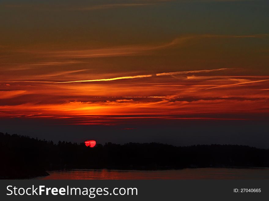 Big purple sun falls behind coastal black forest. Big purple sun falls behind coastal black forest