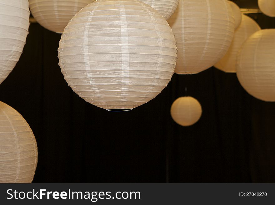 Groupings of various sized paper lanterns hanging against black backdrop