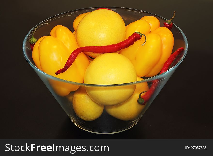 Yellow and red peppers in a glass bowl on a dark background