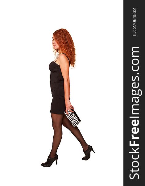 Walking young red-haired woman in black dress and clutch in hand. A side view. Selective focus on woman's face.  Isolated on white background with clipping paths