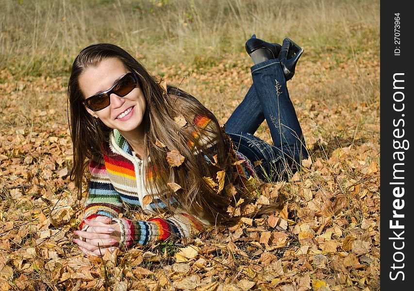 The beautiful smiling young woman lies on yellow autumn leaves. The beautiful smiling young woman lies on yellow autumn leaves