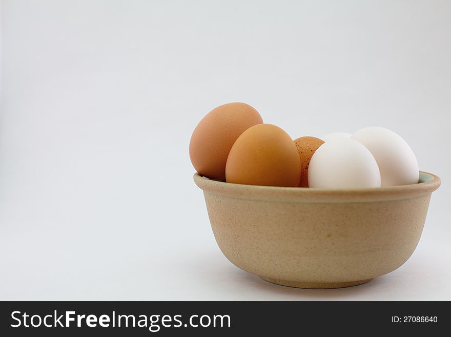 White and brown eggs in bowl on white background
