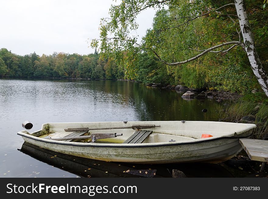 Old glass fiber boat on a lake coast in autumn colors. Old glass fiber boat on a lake coast in autumn colors