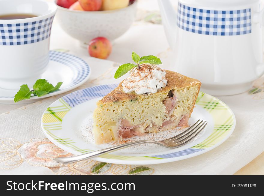 A piece of apple pie, garnished with whipped cream and mint on a plate on the table cloth coverings. A piece of apple pie, garnished with whipped cream and mint on a plate on the table cloth coverings