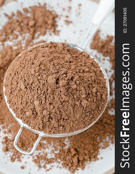 Cocoa powder in a strainer sprinkle on the table close-up