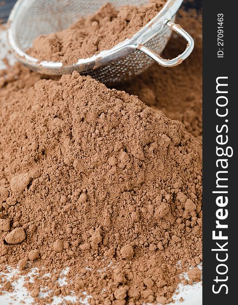 Cocoa powder in a strainer sprinkle on the table close-up