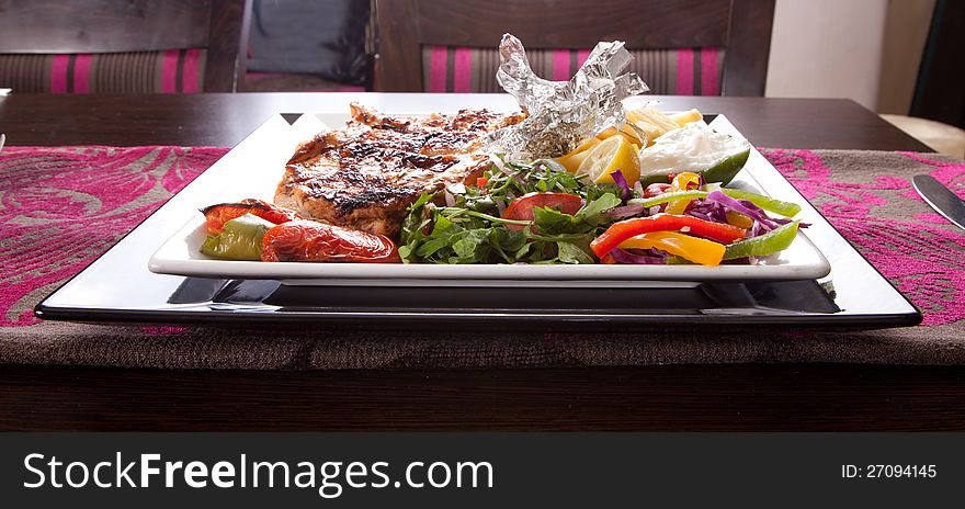 Grilled chicken on a white dish with vegetables on the background. Grilled chicken on a white dish with vegetables on the background.