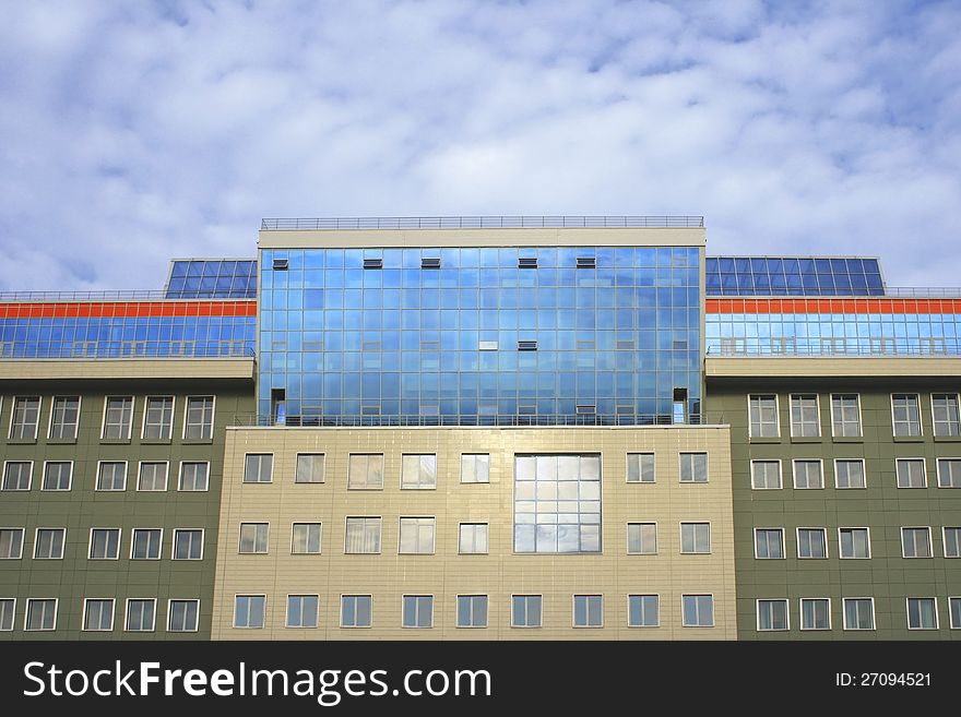 Photo of huge modern business and entertaining building with huge glass and bright orange strip against sky with clouds. Photo of huge modern business and entertaining building with huge glass and bright orange strip against sky with clouds
