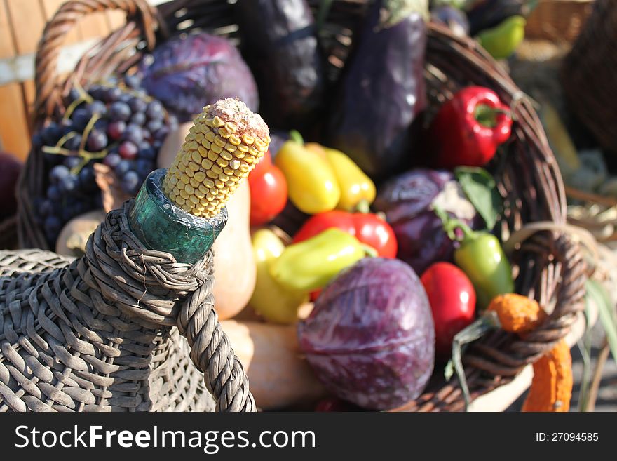 Demijohn with traditional cob stopper - corn cob and autumn vegetables exposed in the basket.