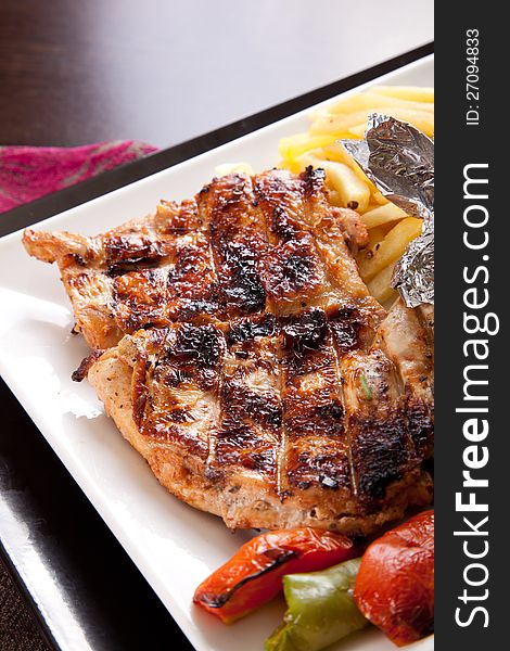 Grilled chicken on a white dish with vegetables on the background.