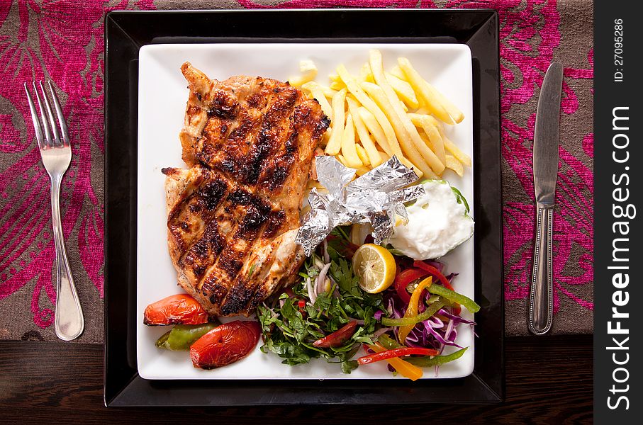 Grilled chicken on a white dish with vegetables on the background.