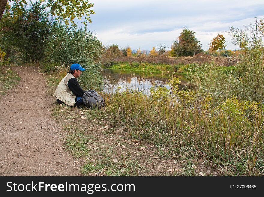 Middle aged man resting on bank of Big Thompson River in Loveland, Co with fishing pole and backpack in Autumn. Middle aged man resting on bank of Big Thompson River in Loveland, Co with fishing pole and backpack in Autumn.