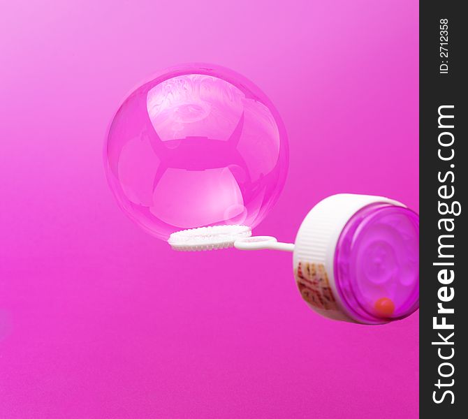 Liquid soap bubble on bubble blower against a pink background