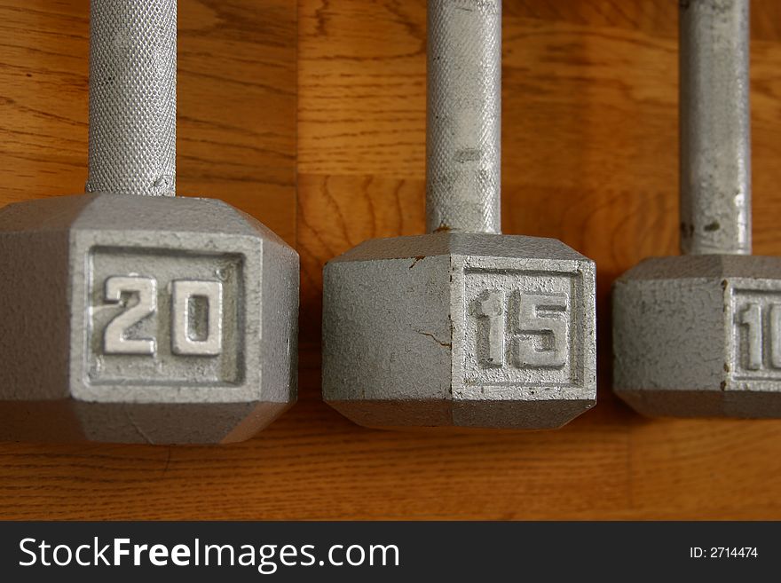 Set of three dumbells on hardwood gym floor with focus on 15 pound center dumbell. Set of three dumbells on hardwood gym floor with focus on 15 pound center dumbell.