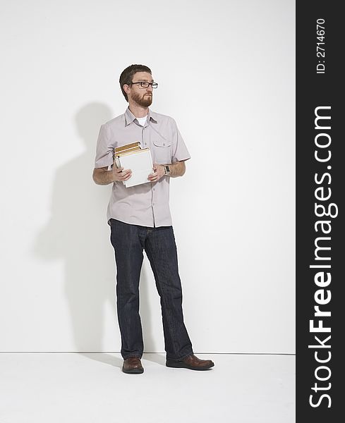 Man in a gray shirt and denim holding a stack of white books standing full length against a white studio wall. Man in a gray shirt and denim holding a stack of white books standing full length against a white studio wall.