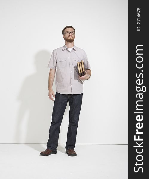 Man in a gray shirt and denim holding a stack of brown books standing full length against a white studio wall. The man is looking up in a thought. Man in a gray shirt and denim holding a stack of brown books standing full length against a white studio wall. The man is looking up in a thought.