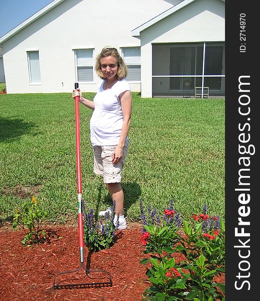 Pregnant woman with a rake in a flower garden. Pregnant woman with a rake in a flower garden.