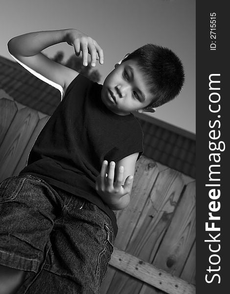 Young asian boy standing outside beside a tall wooden fence wearing jeans and black tshirt. Young asian boy standing outside beside a tall wooden fence wearing jeans and black tshirt