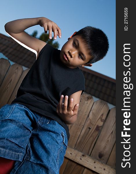 Young asian boy outside beside a tall wooden fence wearing jeans and black tshirt. Young asian boy outside beside a tall wooden fence wearing jeans and black tshirt