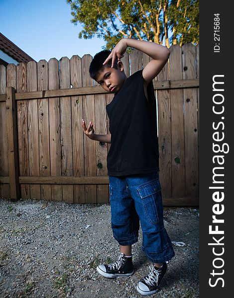 Young asian boy standing outside beside a tall wooden fence wearing jeans and black tshirt. Young asian boy standing outside beside a tall wooden fence wearing jeans and black tshirt