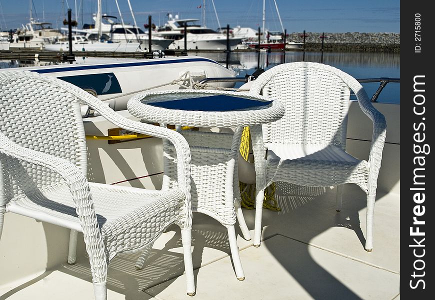 Wicker table and two armchairs at the boat deck prepared to serve lunch with sailboats in the background. Wicker table and two armchairs at the boat deck prepared to serve lunch with sailboats in the background