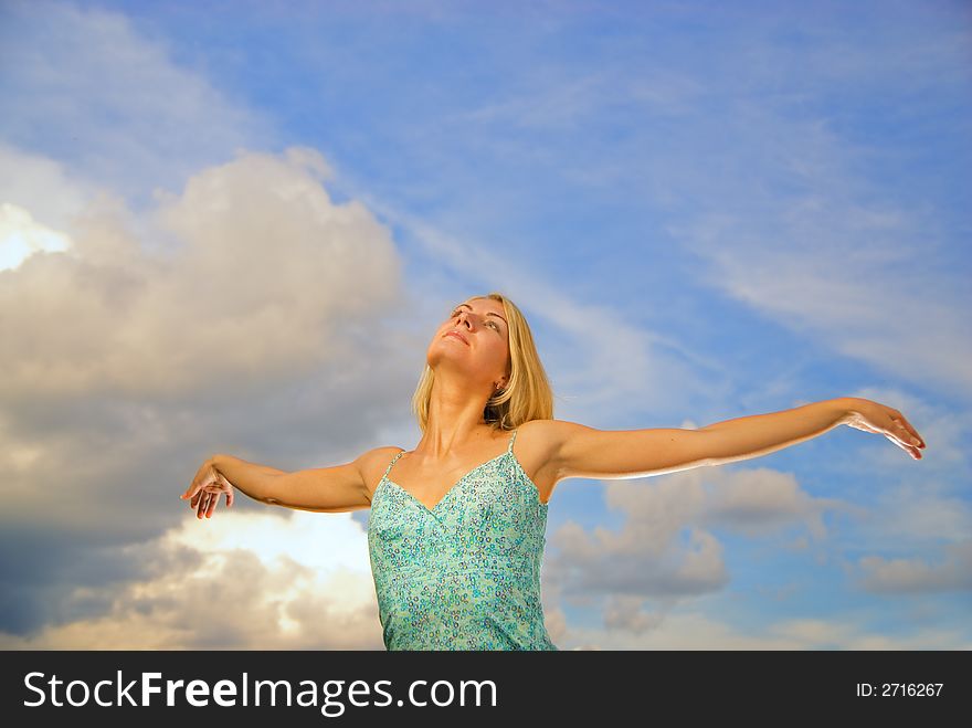 Beautiful blond girl with arms wide open over blue cloudy sky