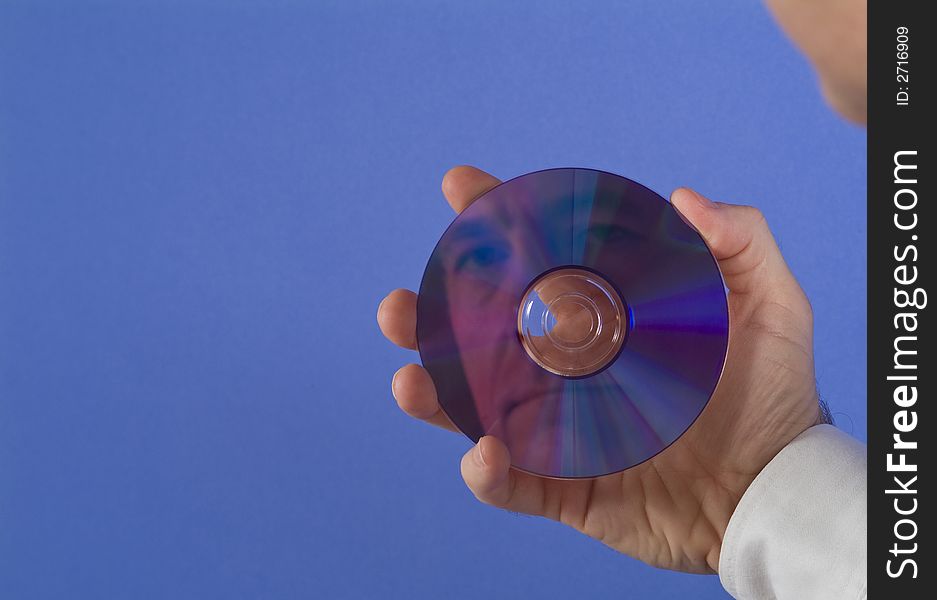 A man holding a DVD or CD with his face reflecting back at him with available copy space. A man holding a DVD or CD with his face reflecting back at him with available copy space.