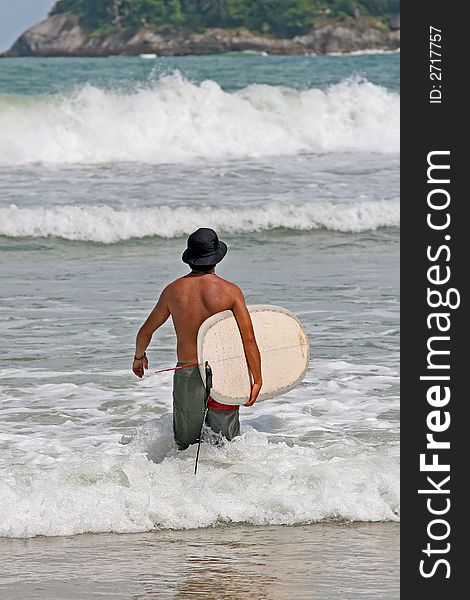 Surfer wearing a hat makes his way into the waves in Phuket, Thailand. Surfer wearing a hat makes his way into the waves in Phuket, Thailand