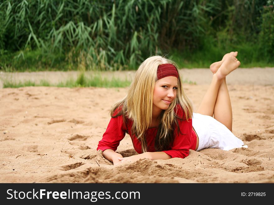A young beautiful woman lying on a beach is smiling. A young beautiful woman lying on a beach is smiling
